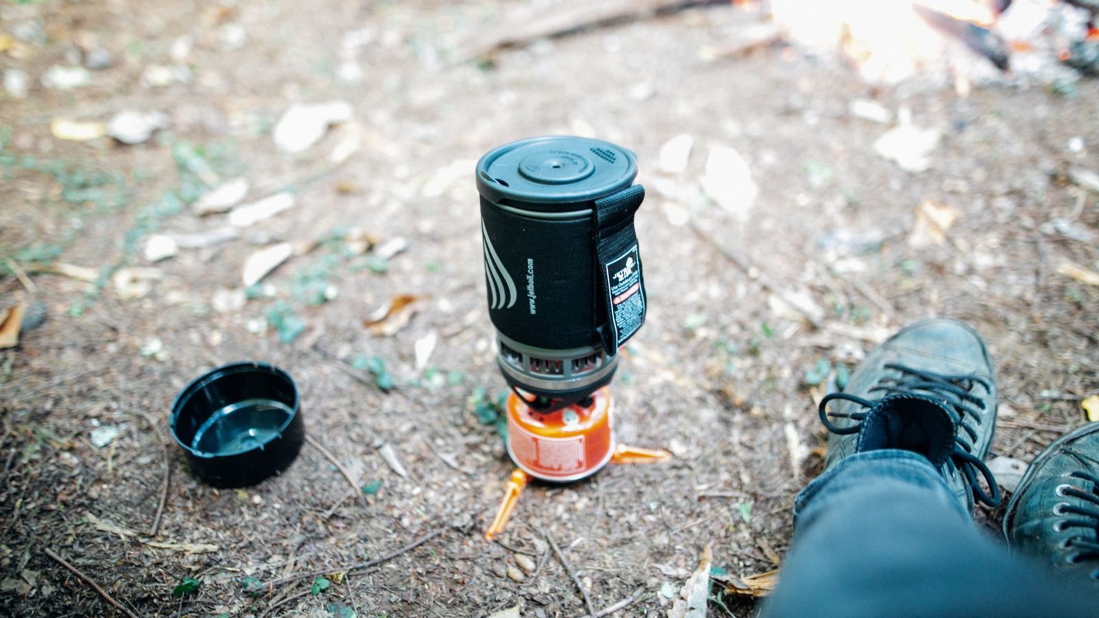 From above of crop anonymous traveler resting in autumn forest near bonfire and lightweight compact camping stove