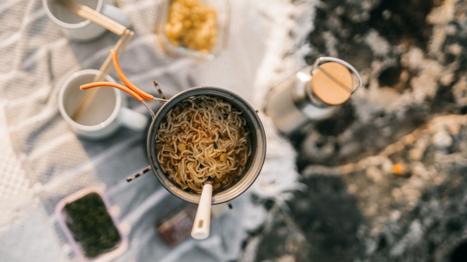 Top view of instant noodles cooking during a camping trip, with various outdoor kitchen essentials.