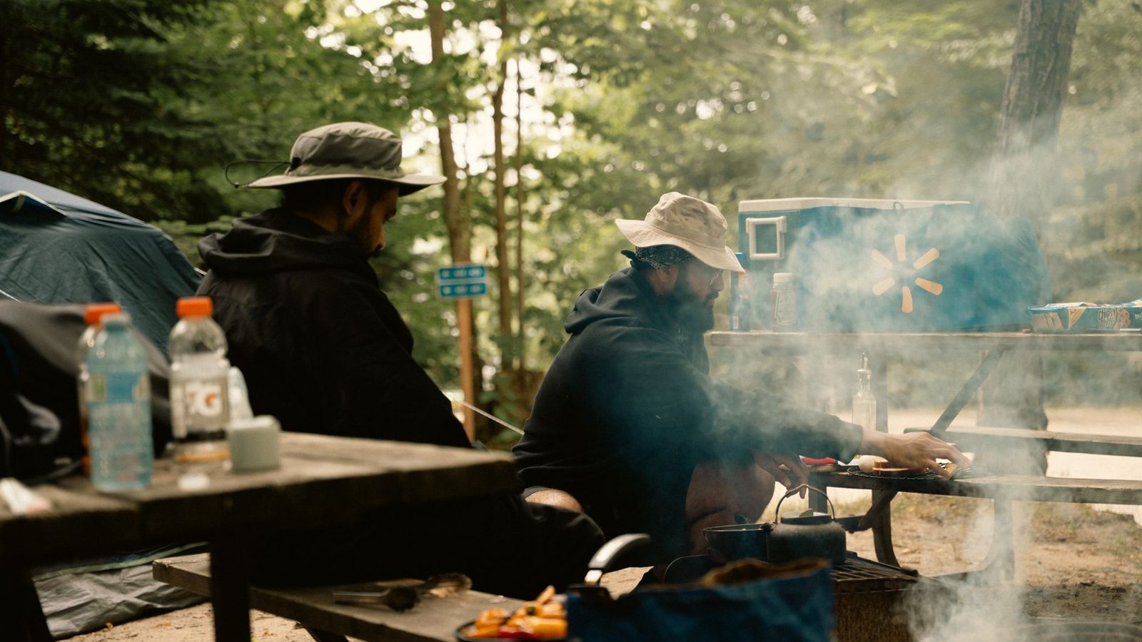 Outdoor camping scene with men cooking at a campsite with tents and trees.