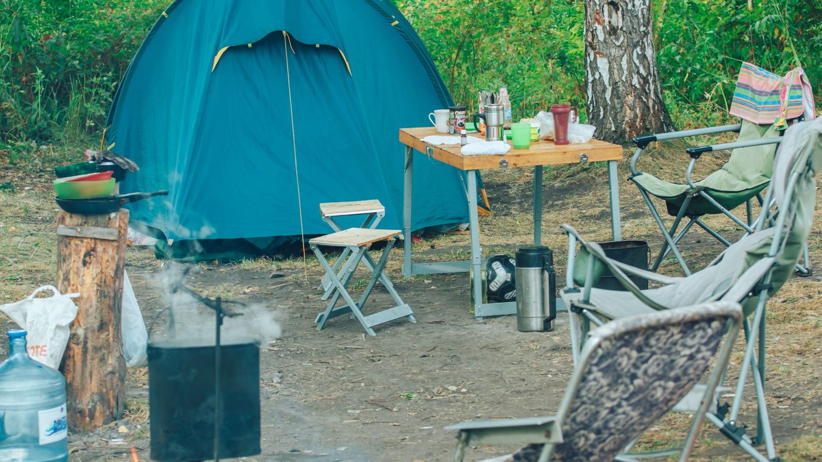 Serene campsite featuring a tent, chairs, and campfire amidst lush greenery for a perfect outdoor adventure.