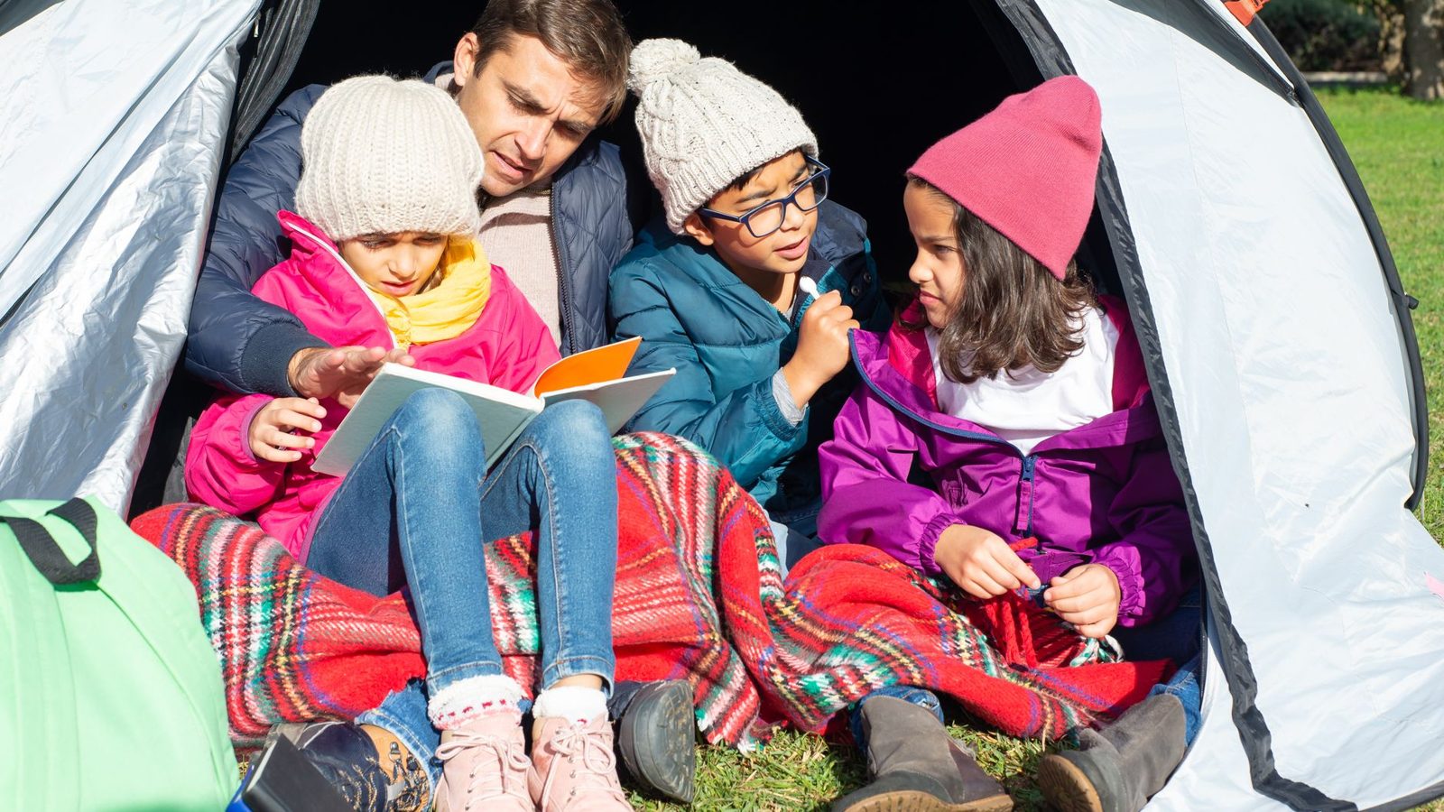 Family enjoying a cozy reading session in a tent during a camping adventure.