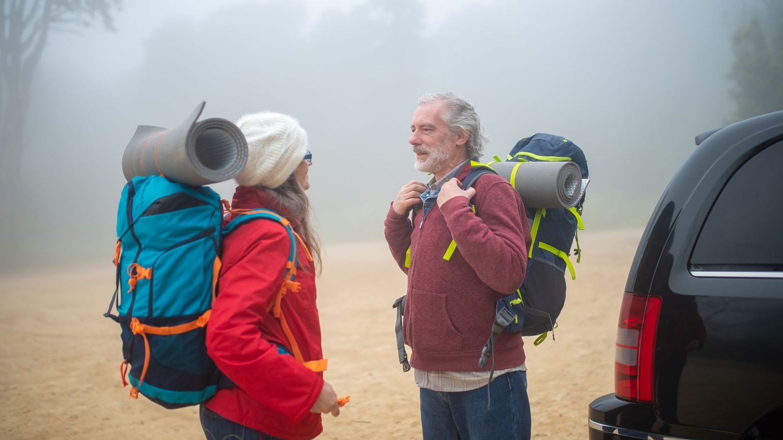 Elderly couple with backpacks getting ready for a hike in foggy Portugal outdoors.