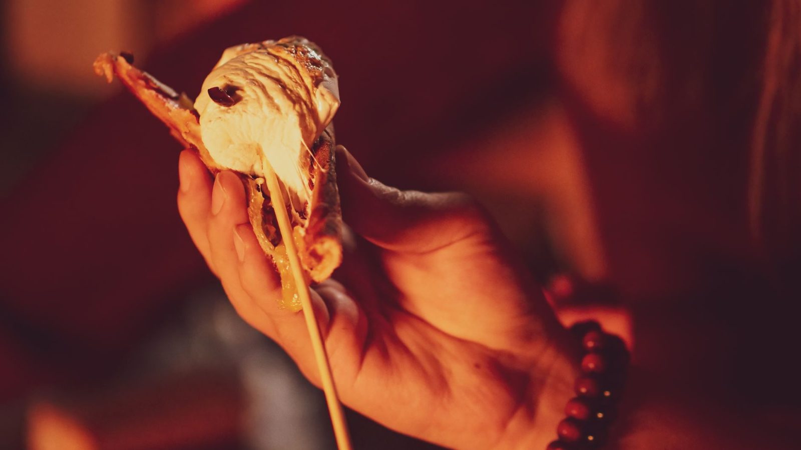 Close-up view of a hand holding a gooey s&rsquo;more with melted marshmallow over a campfire.