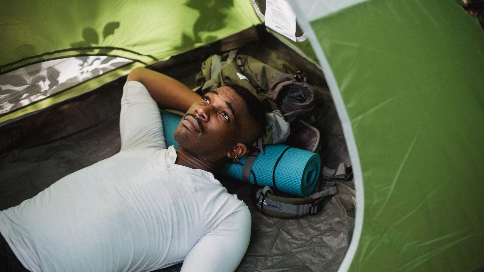 From above of peaceful African American male lying in tent while having break in trekking in nature