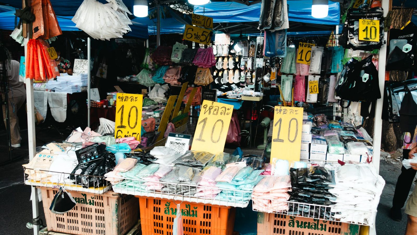 Colorful street market with clothing stalls and sale signs, vibrant and bustling.