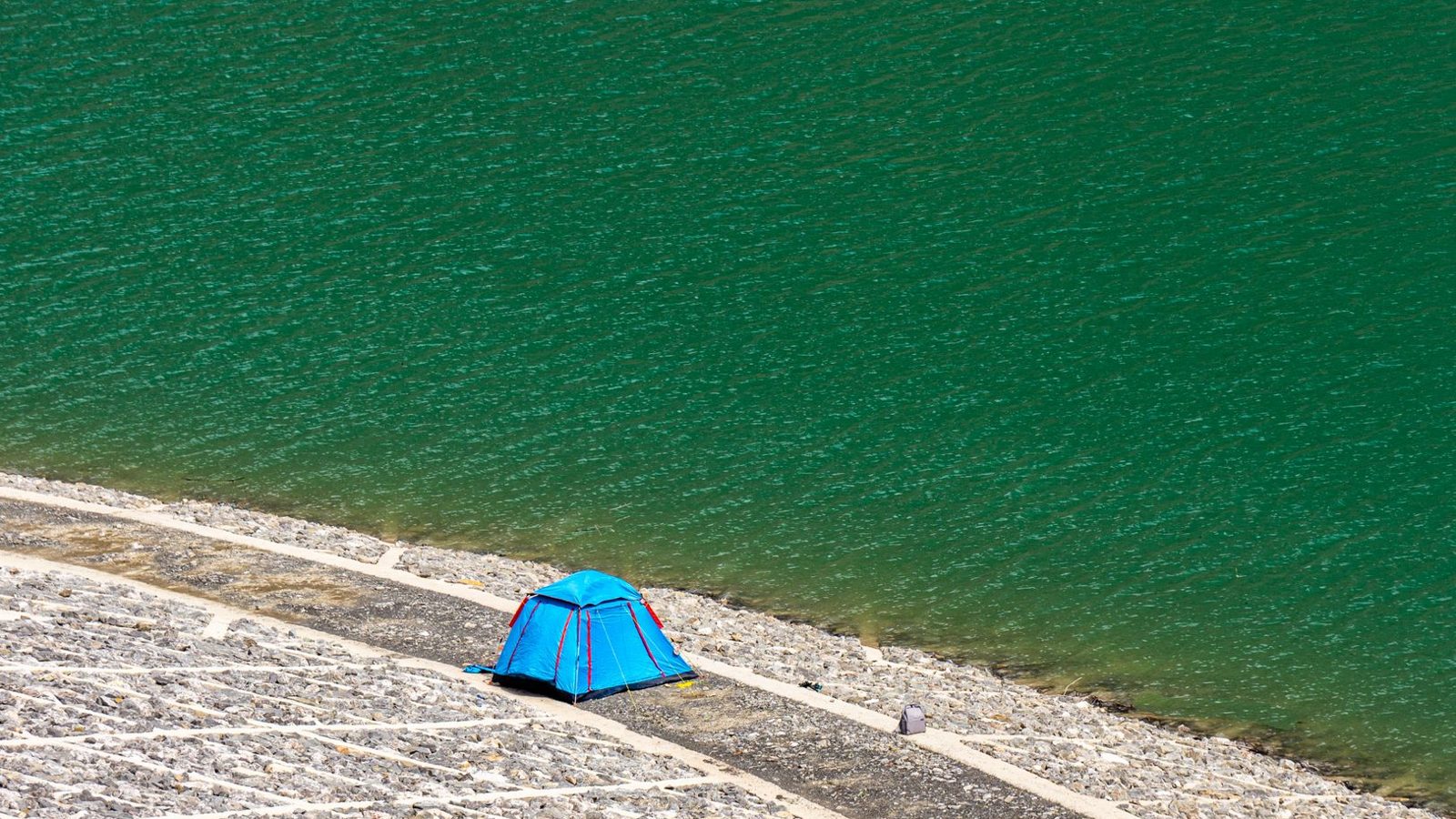 A vibrant blue tent set by the captivating green lake, perfect for a serene camping experience.
