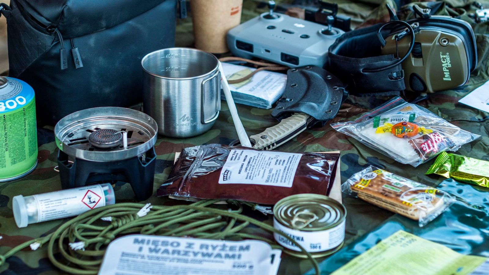 A diverse assortment of camping and survival items laid out, including food, tools, and gadgets.