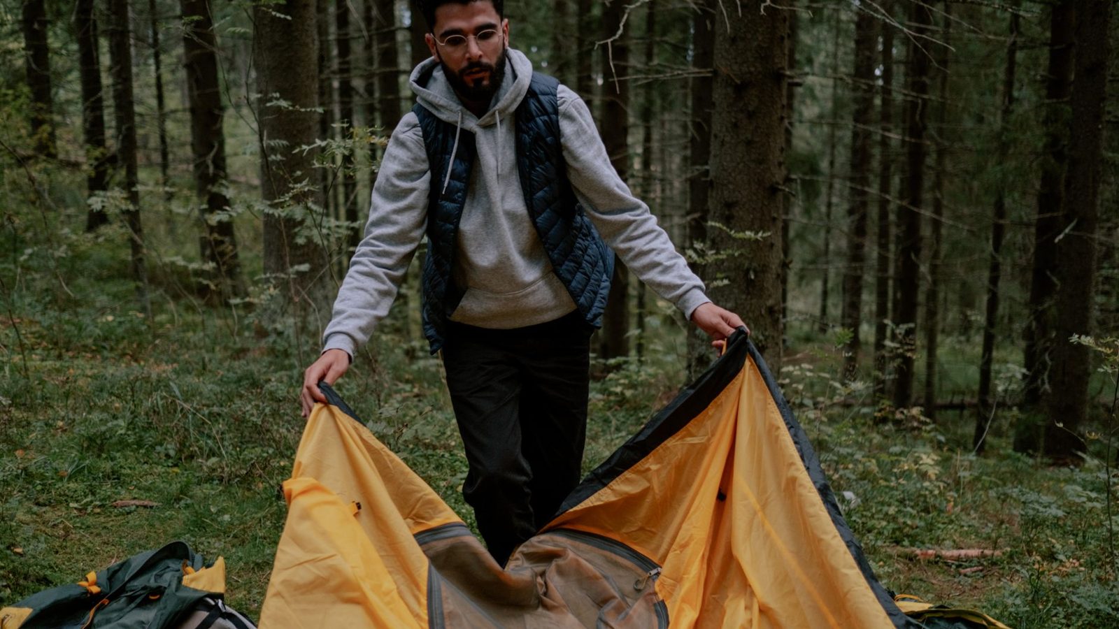 Man setting up a yellow tent in the forest, preparing for camping adventure.